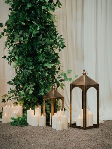 Elegant candles and lanterns beside leafy greenery.