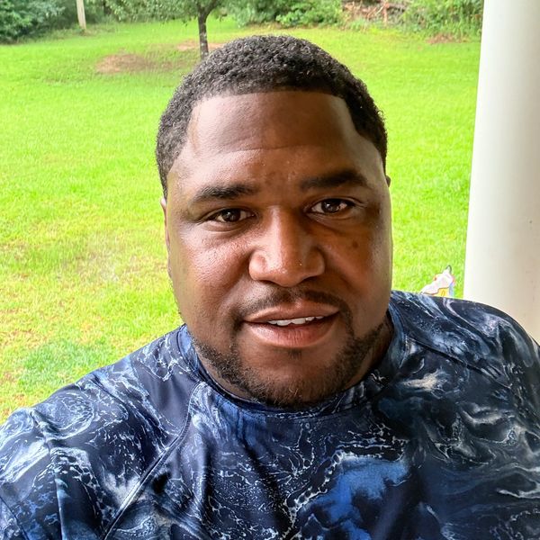 Man smiling outdoors with green trees and grass in the background.