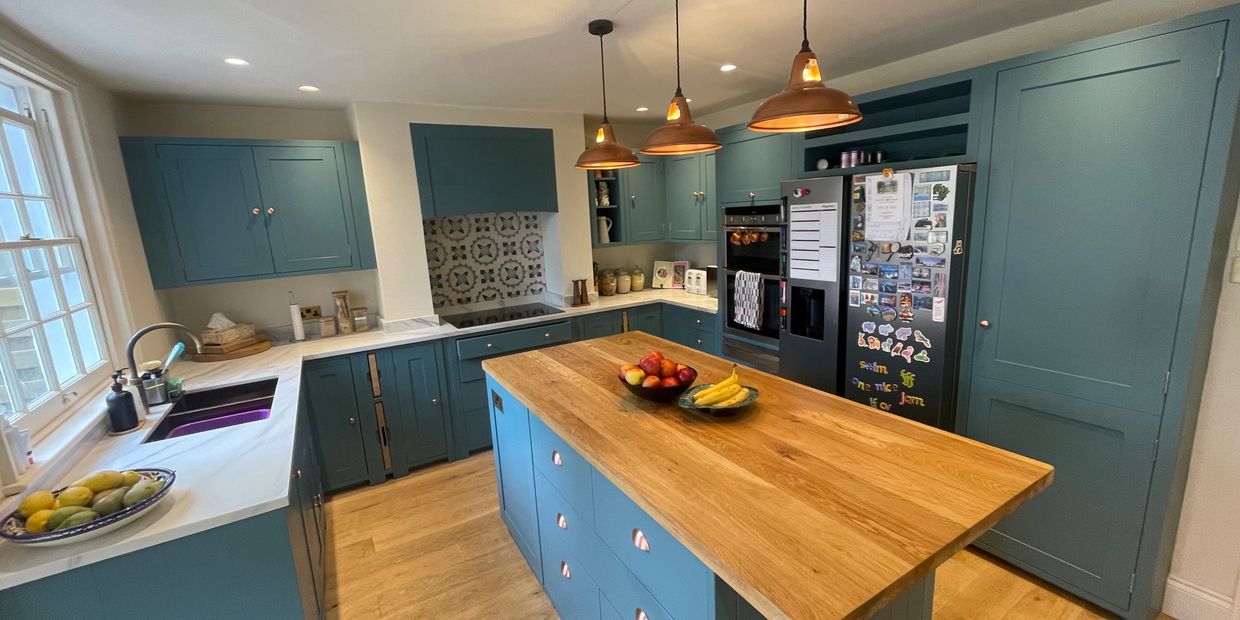 Decluttered and organised modern kitchen with blue cabinets and wooden island under pendant lights.