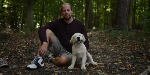 White English cream golden retriever puppy for sale sitting with his best friend in the woods.