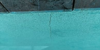 Close-up of a cracked pool edge with water reflecting turquoise hues.