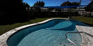 Clear backyard swimming pool with brick patio under bright blue sky.