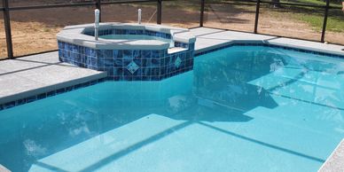 Clear blue swimming pool with attached hot tub under screened enclosure.