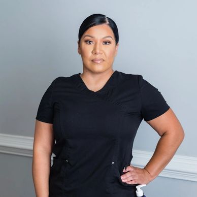 Confident woman in black medical scrubs against a gray wall.