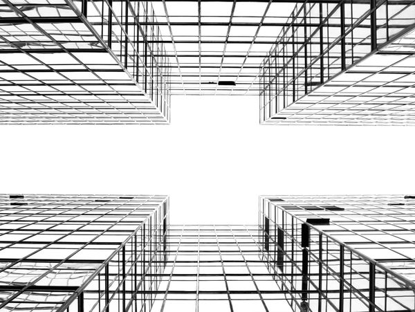 Looking up at symmetrical glass skyscrapers with a bright sky in the center.
