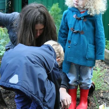 A mother gardening with two children, the young girl wears red wellington boots and a duffle coat