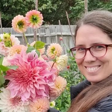 A female flower farmer smiles at the camera, she is holding a bunch of freshly picked dahlias