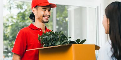 Delivery man in red uniform handing a box with plants to a customer.