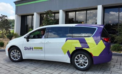 A white and purple Shift on-demand shuttle van parked outside a building.