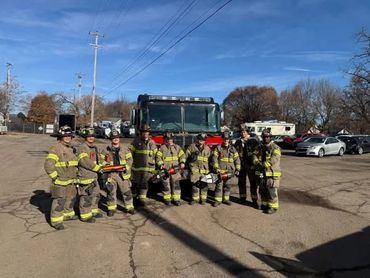 Group of firefighters posing in front of a fire truck on a clear day.