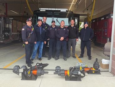 Group of firefighters posing with rescue tools inside a fire station.