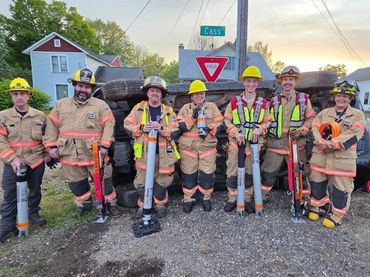 A group of firefighters in gear holding equipment on a street corner.