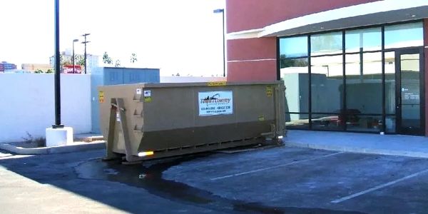 A large dumpster placed in a parking lot outside a commercial building.