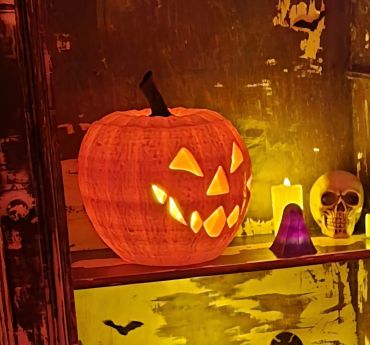 Abóbora de Halloween iluminada ao lado de vela e caveira.