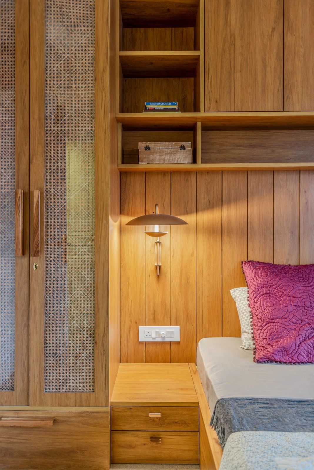 Cozy wooden bedroom corner with built-in shelves and a wall lamp.