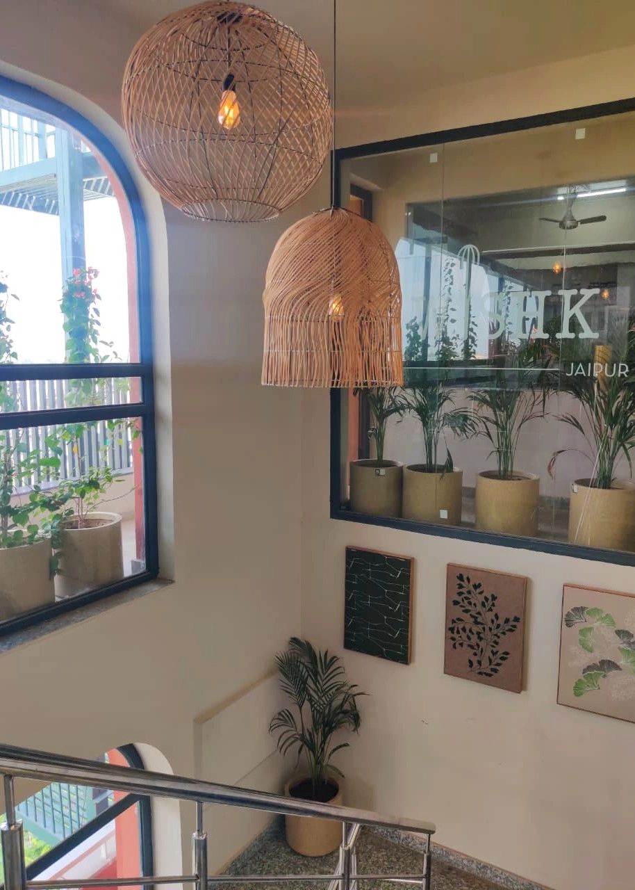 Cozy corner with hanging wicker lamps, potted plants, and artistic wall decor near a staircase.