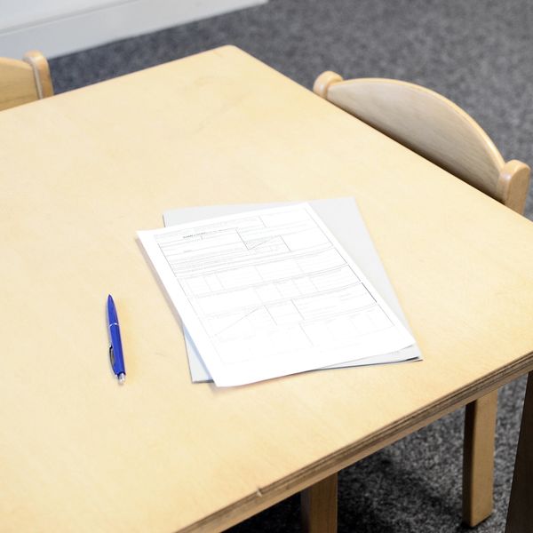 A blue pen and papers on a wooden table with chairs.