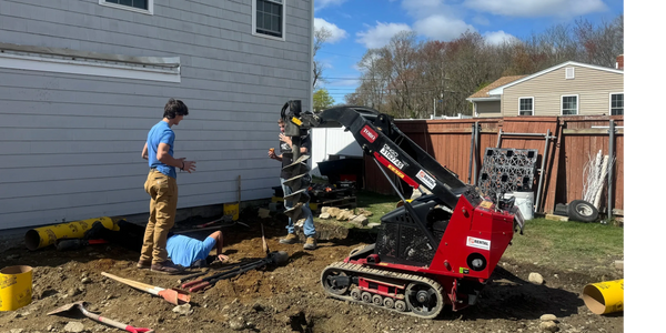 Three men working with a red Toro Dingo machine at a construction site beside a house.