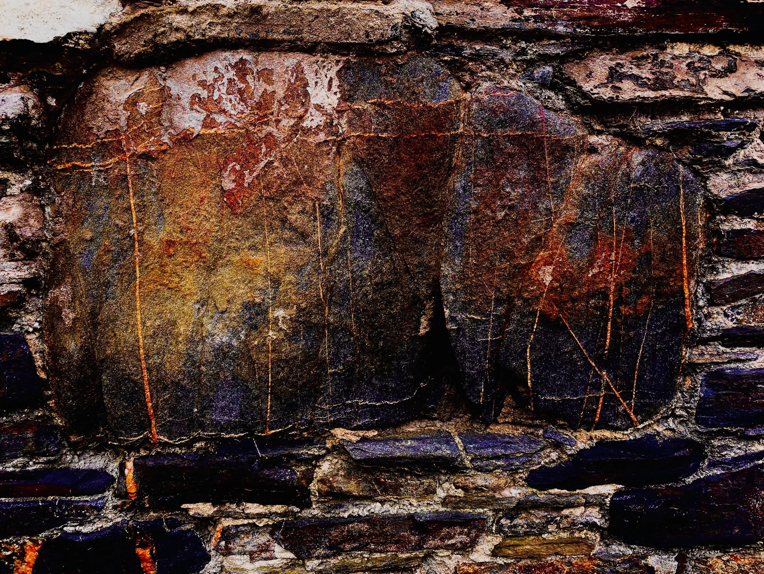 Close-up of textured, colorful rock surface with dark and rusty hues.