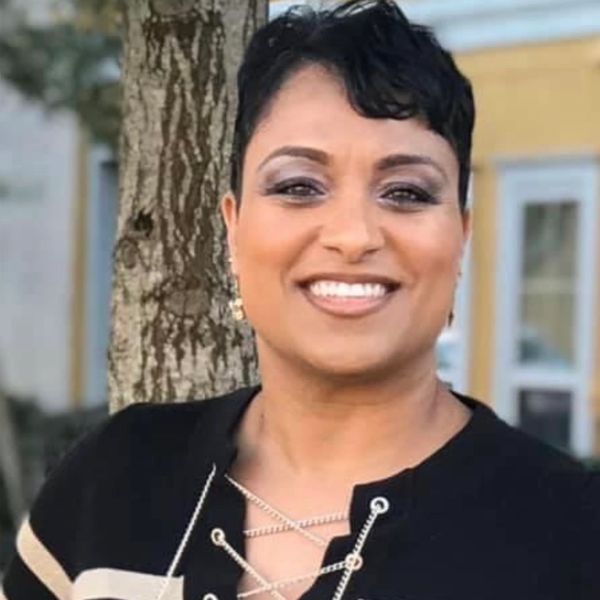 Smiling woman with short hair standing outdoors near a tree.