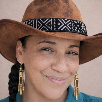 Woman wearing a brown cowboy hat with patterned band and gold earrings.