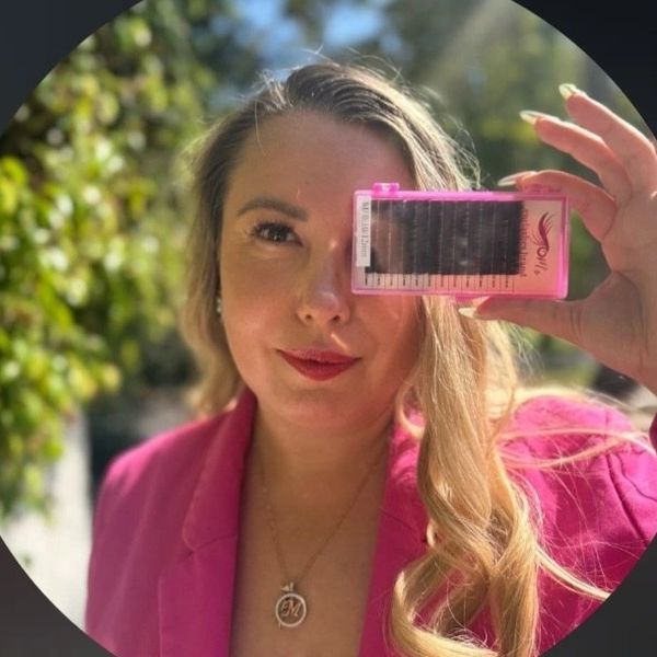 Woman in pink jacket holding a pink eyelash extension tray outdoors.
