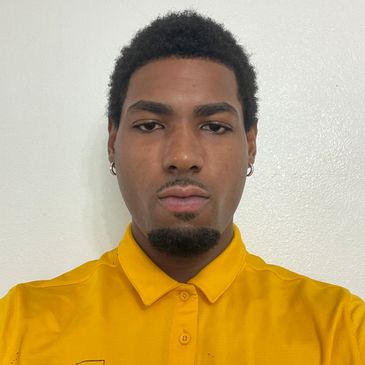Man with short curly hair wearing a yellow collared shirt.