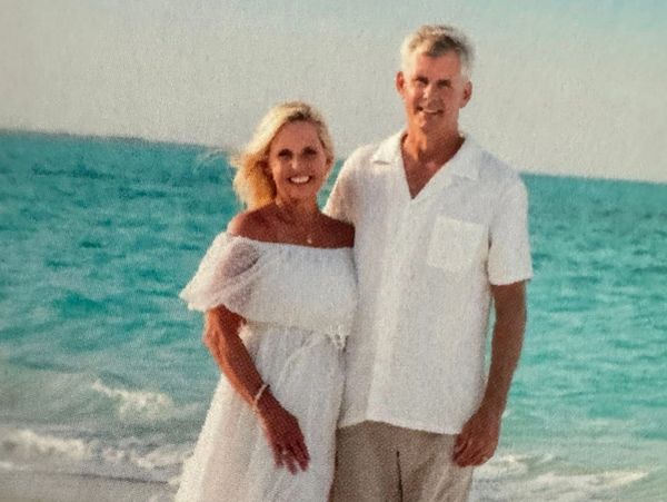 Couple standing on a beach with ocean background.