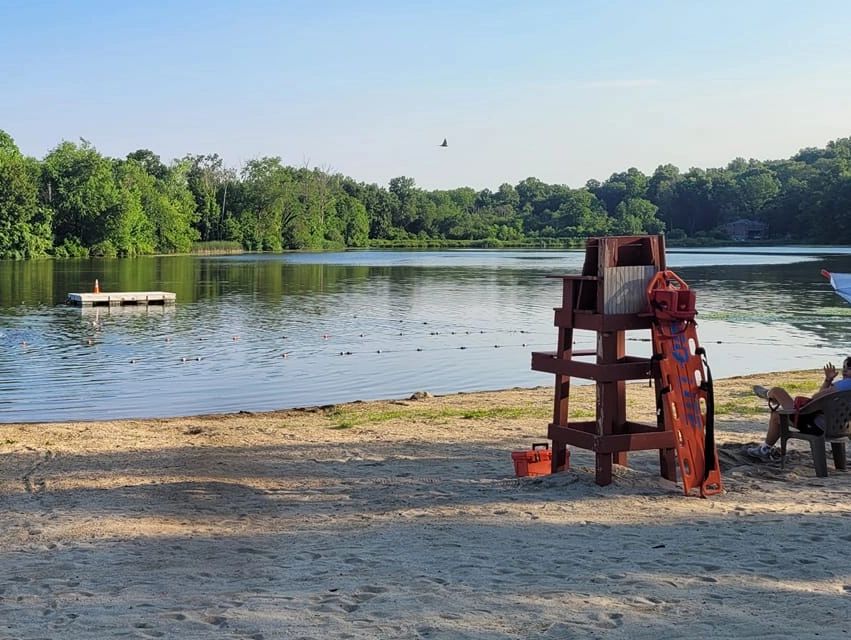 A serene lakeside beach with a lifeguard chair and floating dock.