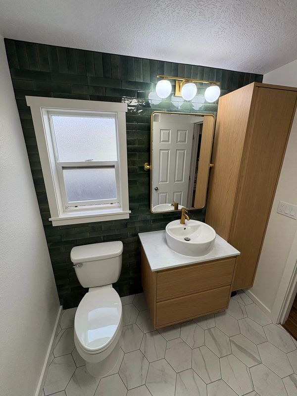 Modern bathroom with green tiles, wooden vanity, and white toilet.