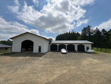A white car parked outside a large white garage under a partly cloudy sky.