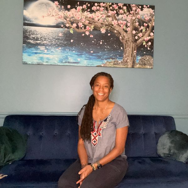 Smiling woman sitting on blue couch beneath cherry blossom painting.