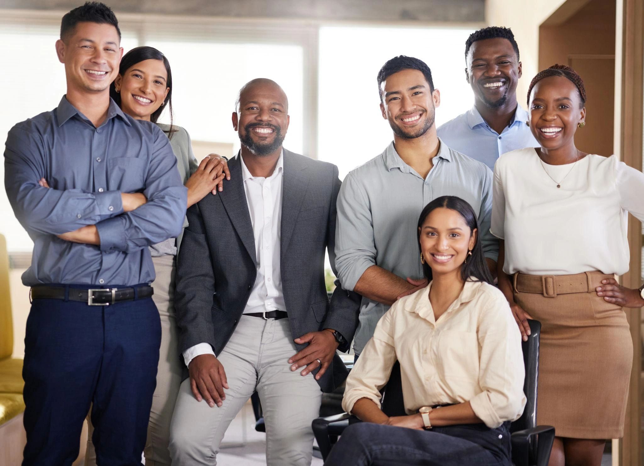 Smiling diverse group of seven professionals posing in an office.