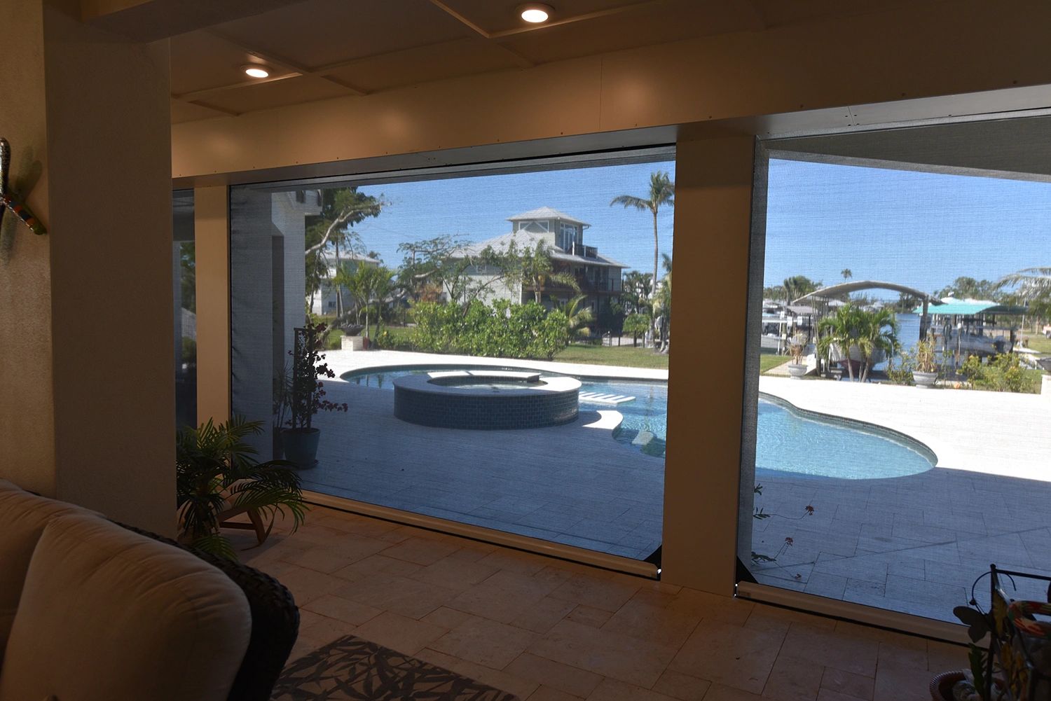 View of a backyard pool and hot tub through screened patio windows.