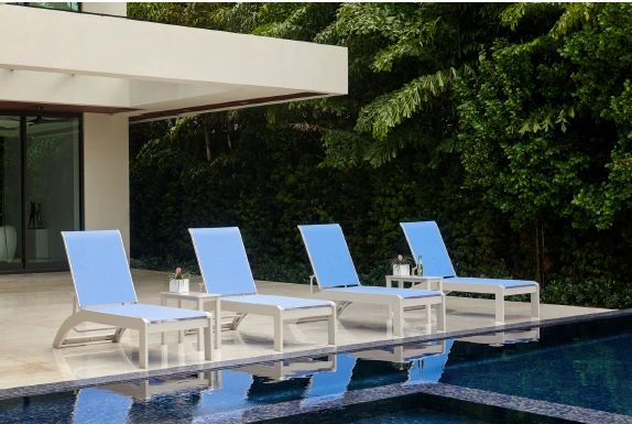 Four blue lounge chairs beside a clear swimming pool with lush greenery in the background.