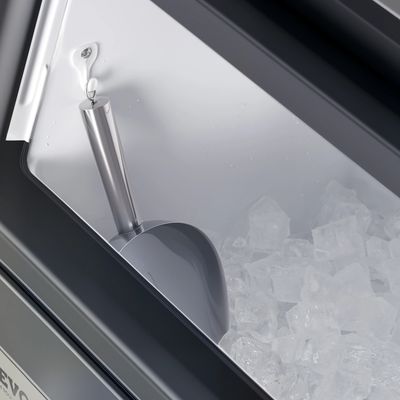 Close-up of an ice scoop resting on ice cubes inside an ice maker.