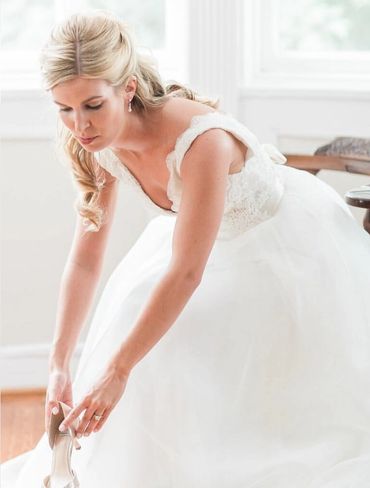 Bride sitting down leaning over putting on high heel shoe