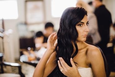 Bride prepping her dark hair looking at herself in the mirror.