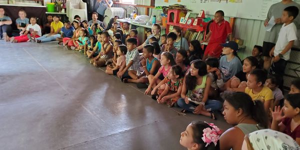 A large group of children and adults sitting on the floor in a classroom, attentively watching something.