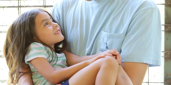 Young man holding a smiling little girl in his arms, sharing a loving moment.