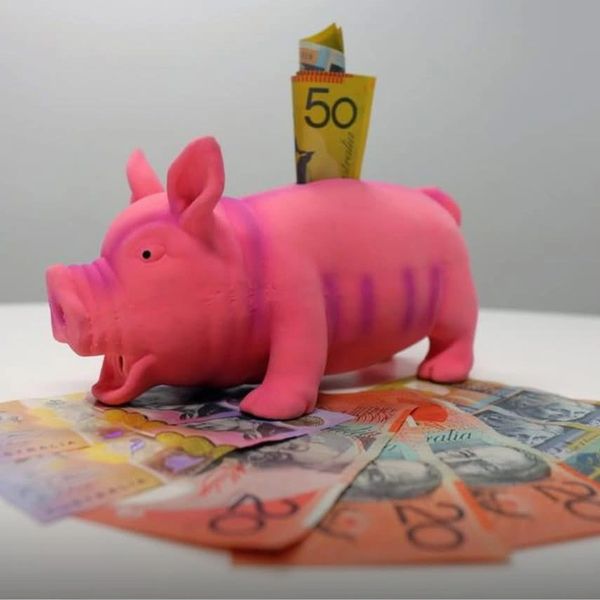 Pink piggy bank with cash inserted and Australian banknotes spread around.