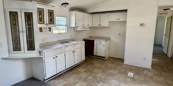 Empty kitchen with white cabinets and tiled floor.