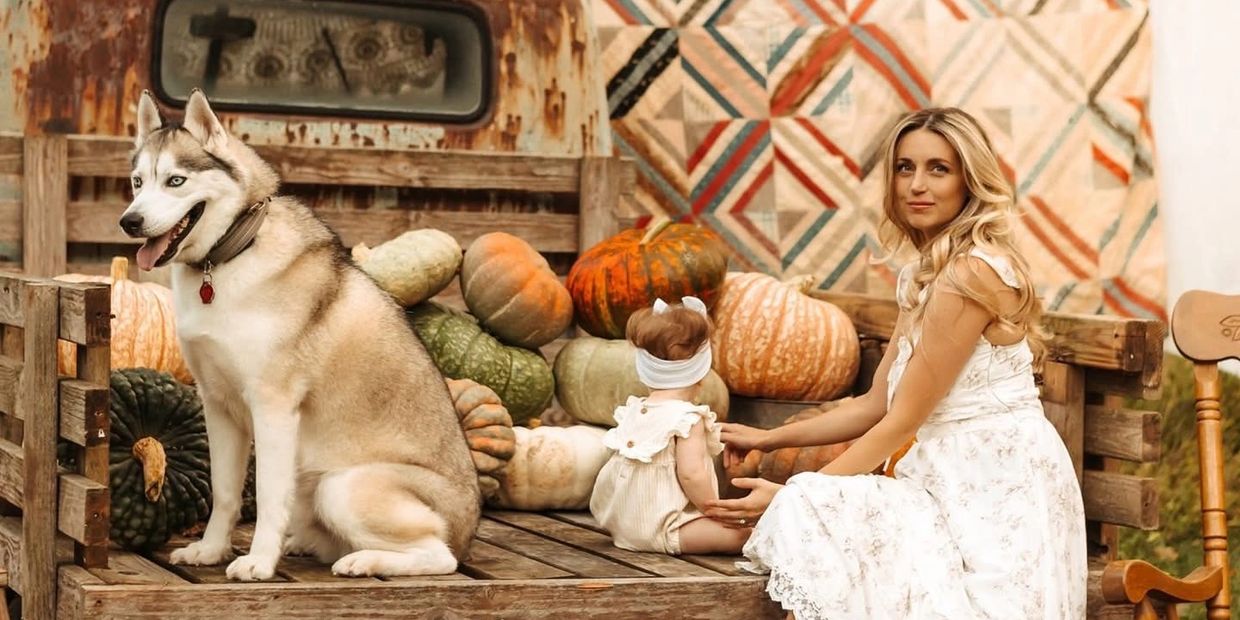 Woman and baby with dog and pumpkins on rustic truck bed in autumn.