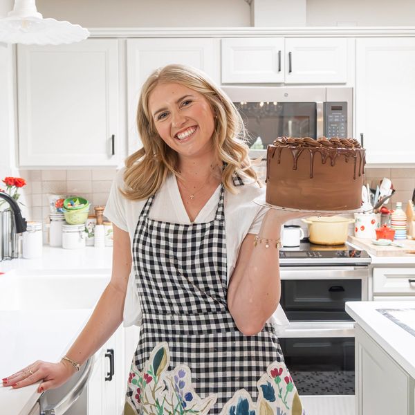 Woman in checkered apron holding a chocolate cake in a kitchen.