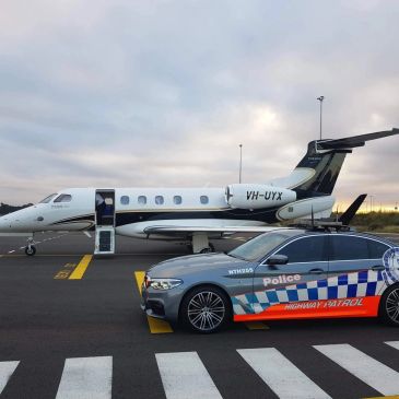 Police car beside a private jet on runway.