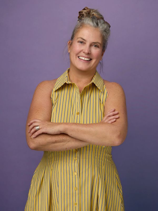 Smiling woman in a yellow striped dress with arms crossed.