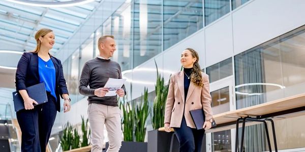 Three professionals walking and talking in a modern office space.
