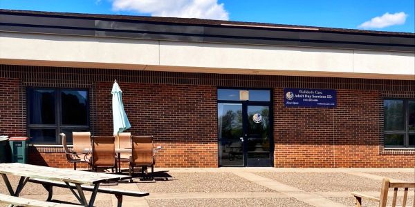The outdoor entrance of Wellderly on a blue sky day. door C the patio with outdoor tables and benche