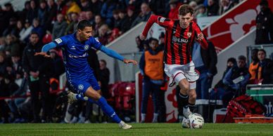 Soccer players in action during a night game with a crowd watching.