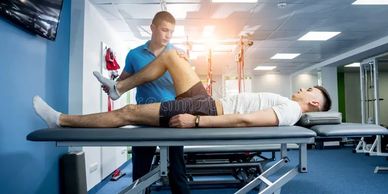 Therapist assists patient with leg stretching exercise in clinic.